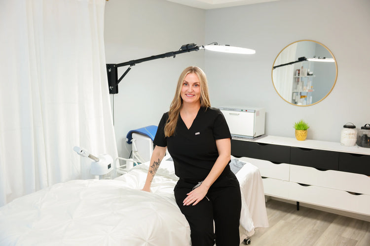 Licensed esthetician in Bedford, NH smiling in a bright, modern skincare treatment room with facial equipment.