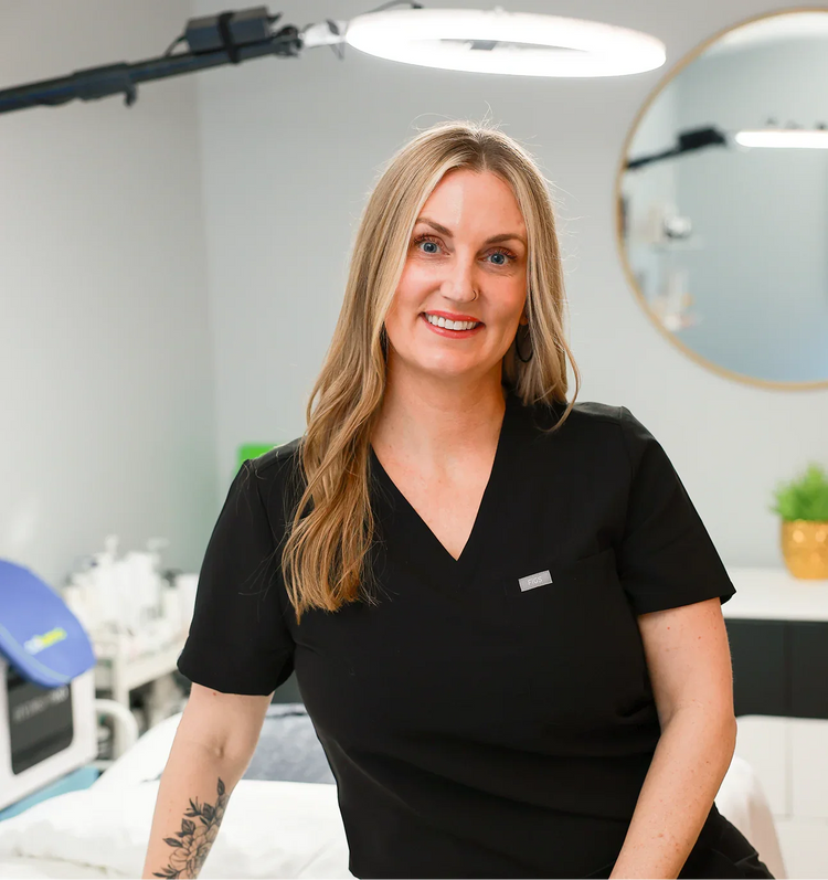 Smiling esthetician in black uniform in a modern skincare treatment room with facial equipment.