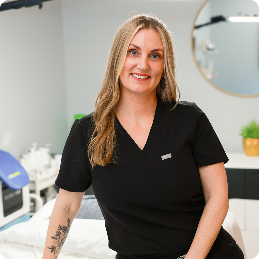 Woman in a black scrub top sitting in a medical or clinical setting.