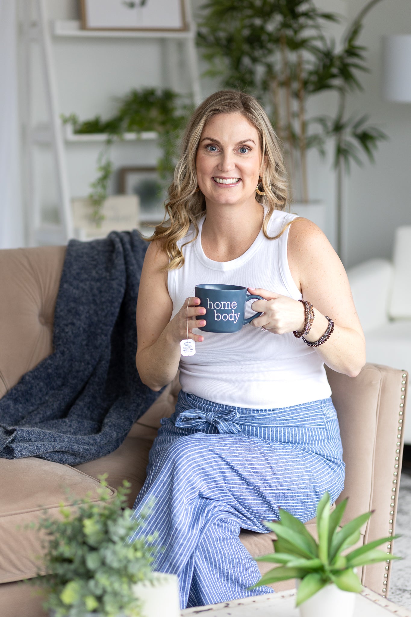 Molly sitting on a couch holding a mug with plants and decor in the background